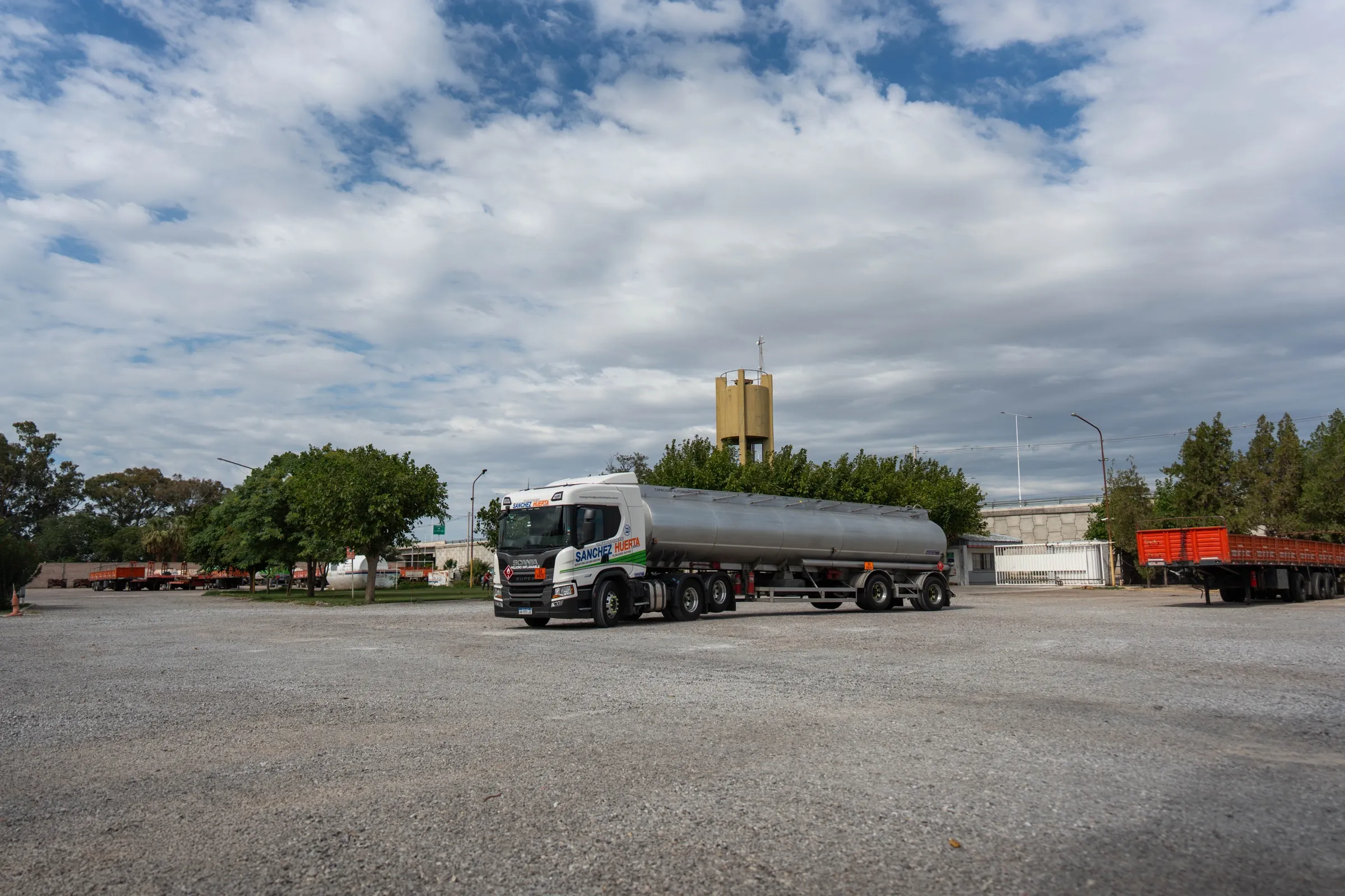 Tractor Scania de Transporte Sanchez Huerta remolcando un semirremolque cisterna de acero inoxidable para transporte de combustibles, con rombo de inflamable y panel de peligro, estacionado en un predio con más semirremolques al fondo