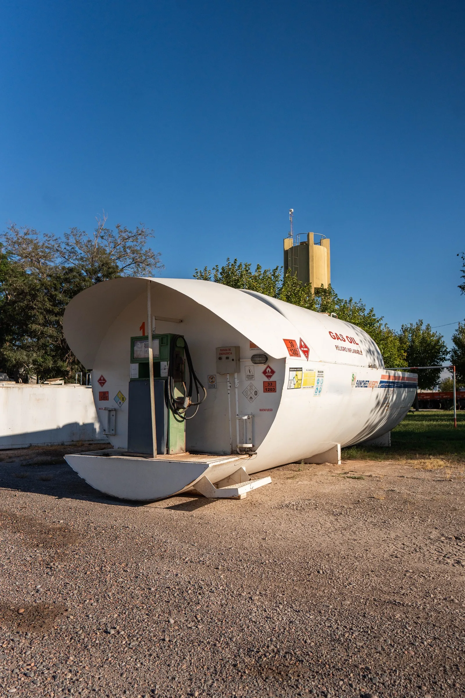 Planta de combustible aérea de Transporte Sanchez Huerta, unidad número 1, con detalle del surtidor, la manguera y la señalización de peligro inflamable 33/1203, bandeja de contención en la base y un silo al fondo